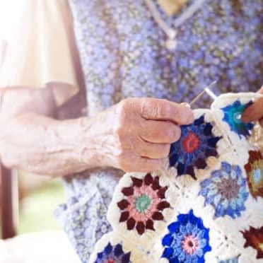Old woman is knitting a blanket inside in her living room
